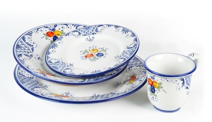 Toscana Blu place setting. Set against a luminous white background, the items' design unfolds with graceful cobalt-blue scrolls interspersed with small, vibrant clusters of hand-painted fruit—rich red cherries, golden apricots, and deep blue plums—accented by soft green leaves.